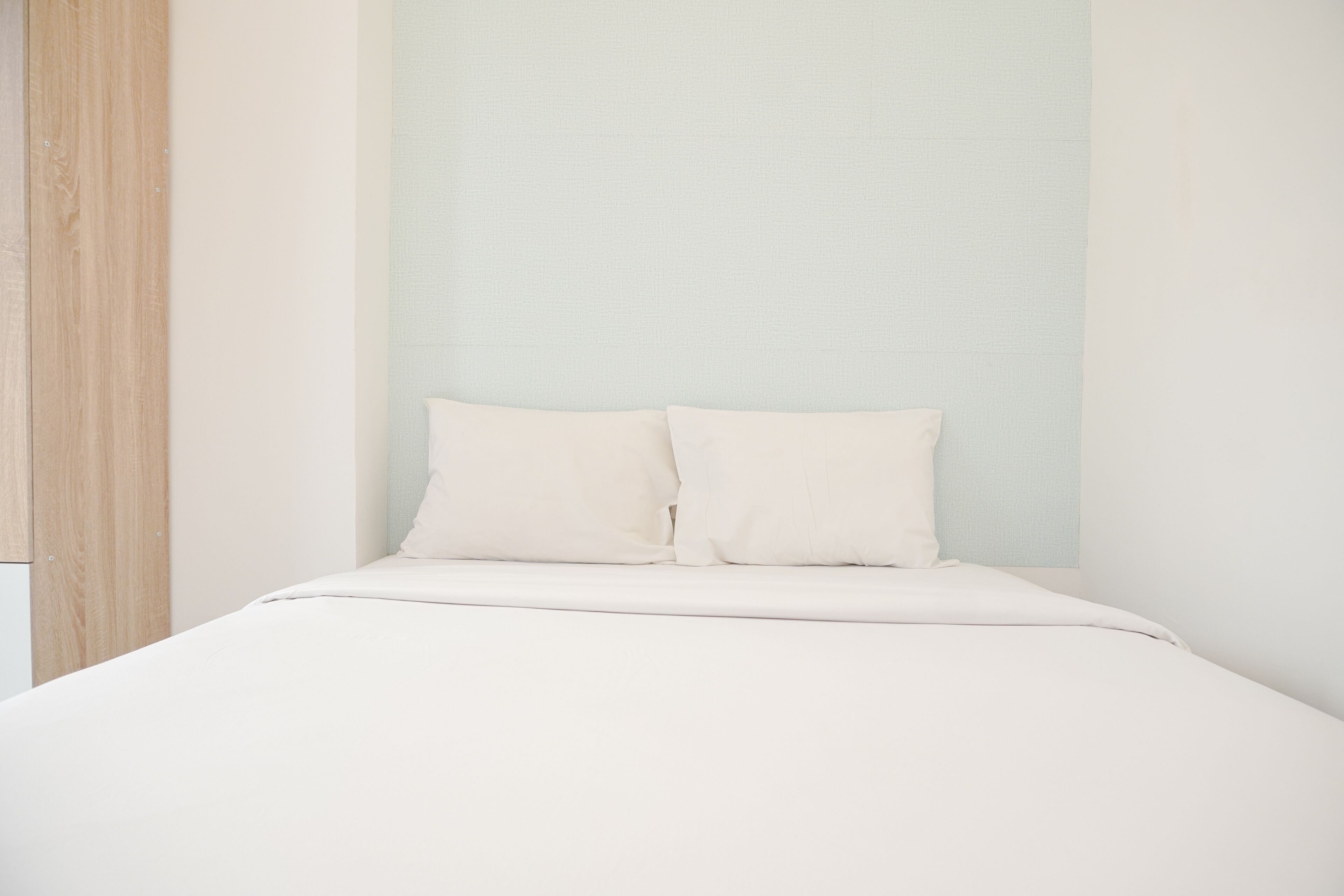 Un dormitorio minimalista con una cama, dos almohadas y una pared de color claro.
