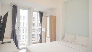 Una habitación de hotel con cama, escritorio, armario y ventana con cortinas.