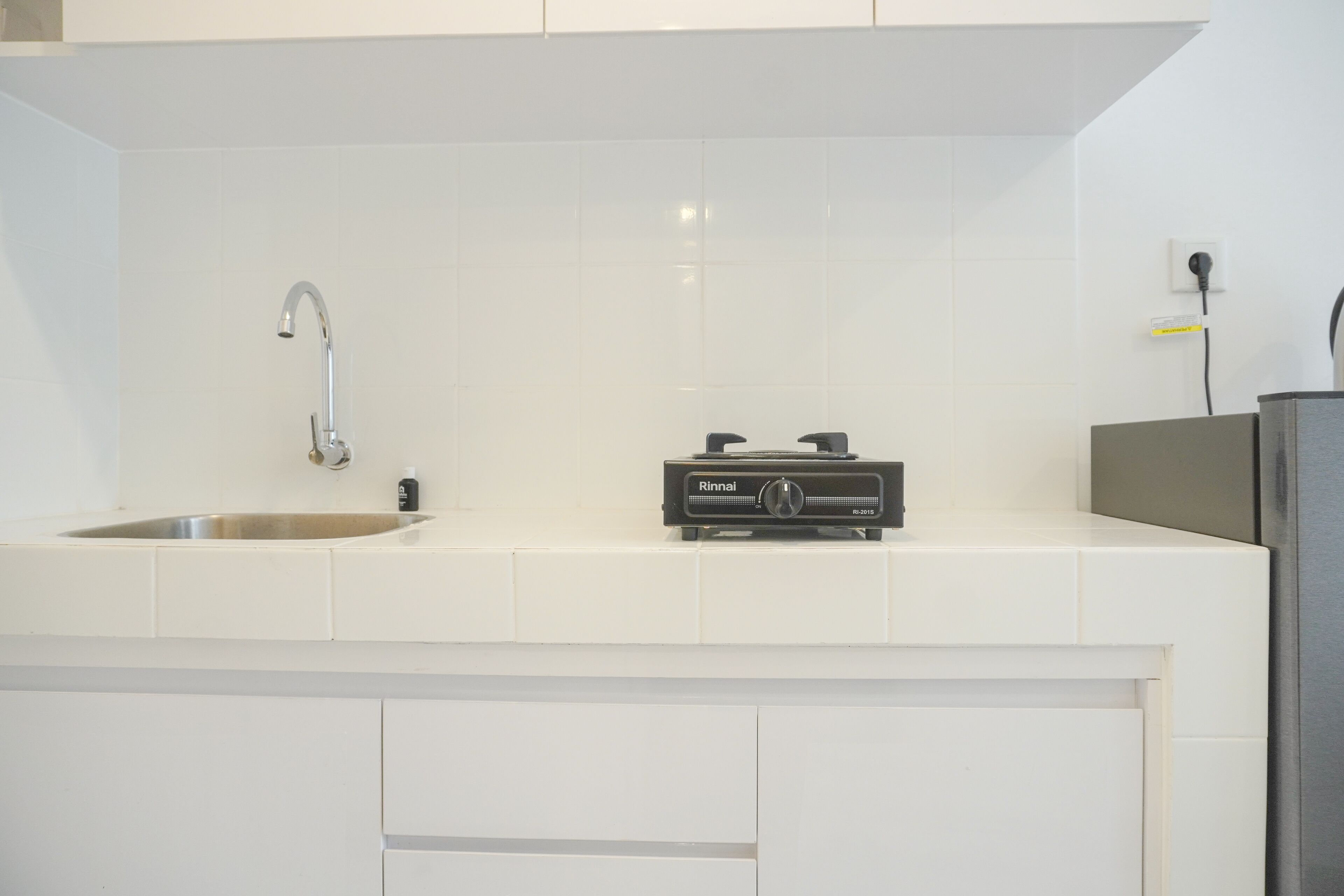 Une cuisine avec des armoires blanches, un évier en acier inoxydable, une cuisinière à gaz Rinnai et une prise électrique au mur.