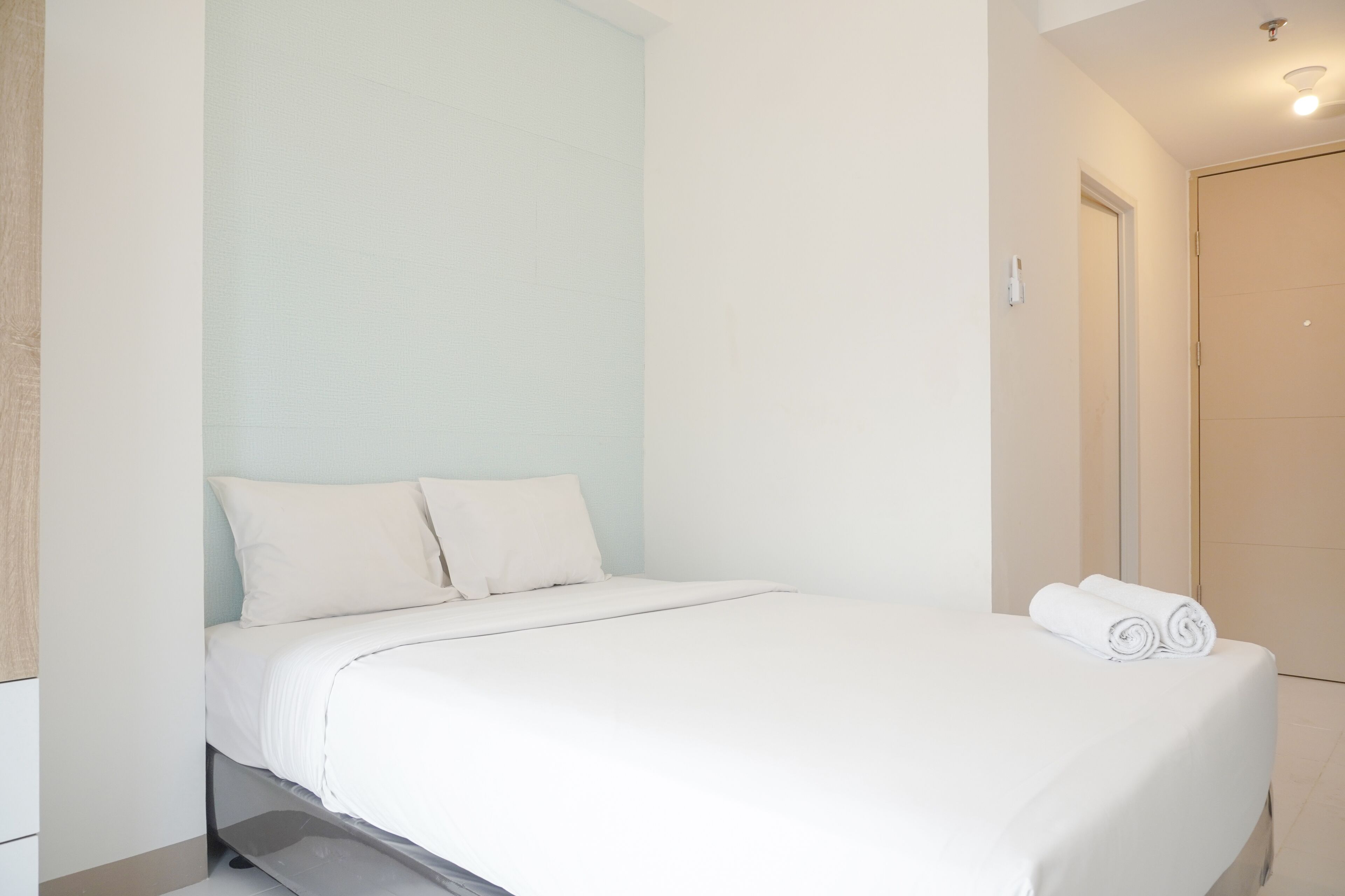 A neatly made bed with white linens and pillows, a small bedside table, and a rolled towel on the bed.