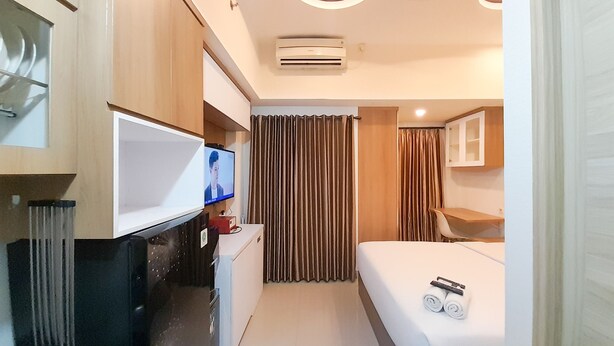 A modern hotel room with a flat-screen TV, a desk with a computer, a bed with rolled towels, and a bathroom with a mirror and sink. - Relaxing Studio At Taman Melati Sinduadi Apartment (Pogung Lor)