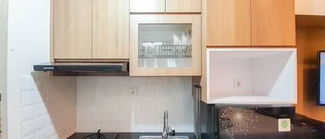 A compact kitchen with wooden cabinets, a black countertop, a stainless steel sink, and a black refrigerator with a green sticker.