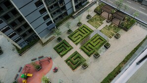 An aerial view of a courtyard with geometric garden beds, a playground, and a building with balconies.