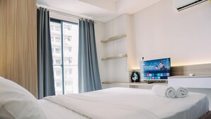 A hotel room with a bed, a TV, a clock, and a window with curtains.