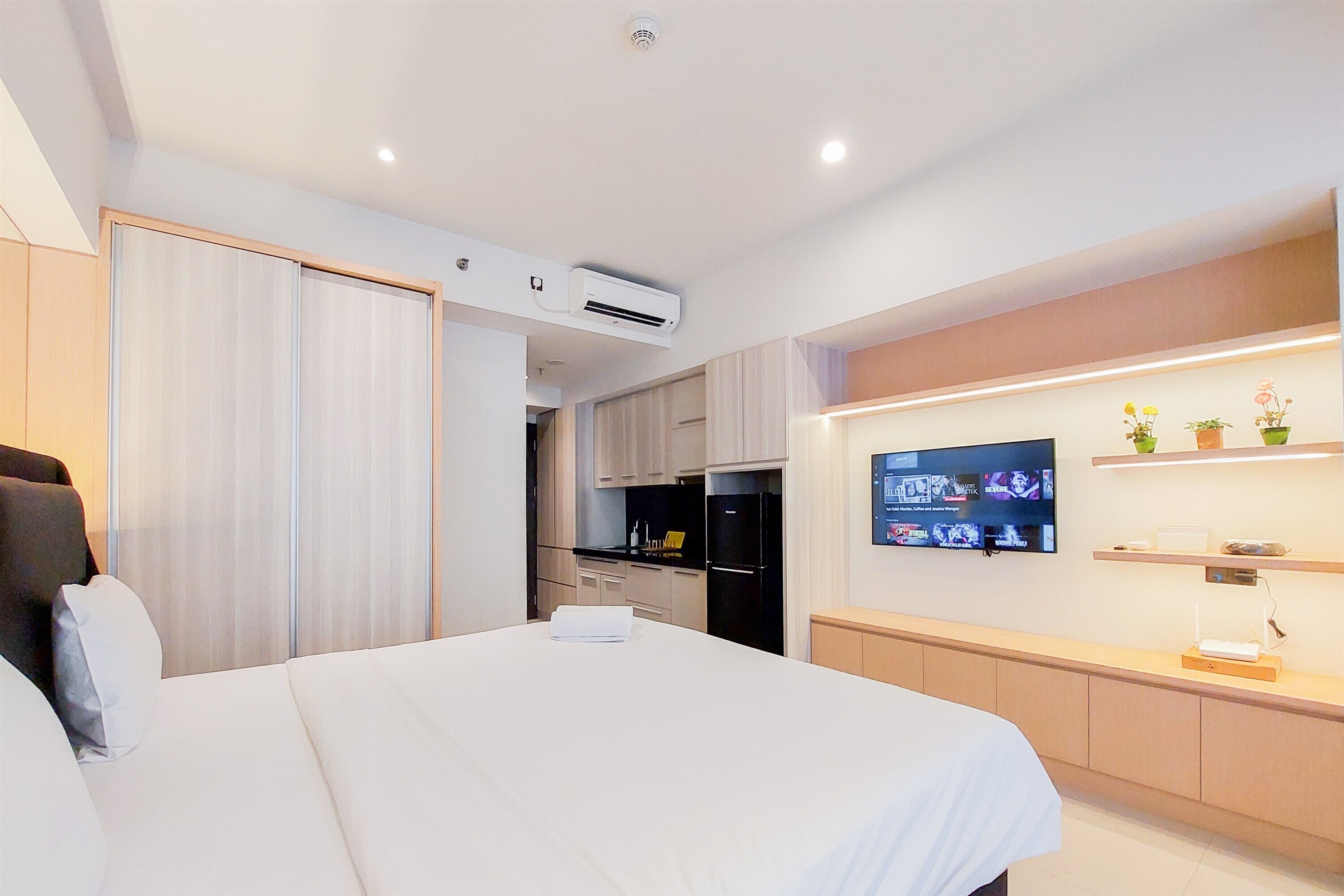 Ein modernes Hotelzimmer mit einem großen Bett, einem an der Wand montierten Fernseher, einer Küchenzeile und einem Schiebetürenschrank.