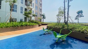 A rooftop terrace with a blue floor, green chairs, and a building with multiple balconies. - Spacious And Homey 1Br Tokyo Riverside Pik 2 Apartment (Teluknaga)