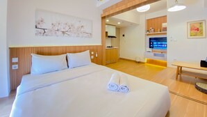 A hotel room with a large bed, a wooden headboard, a wall-mounted air conditioner, a television, and a small table. - Spacious And Homey 1Br Tokyo Riverside Pik 2 Apartment (Teluknaga)