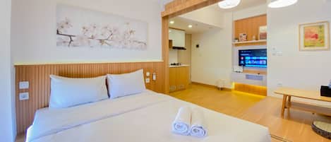 A hotel room with a large bed, a wooden headboard, a wall-mounted air conditioner, a television, and a small table.