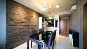 A modern dining area with a glass table and chairs, a stone accent wall, and a chandelier. - Spacious And Comfy 2Br Apartment At Aryaduta Residence Surabaya (Surabaya)