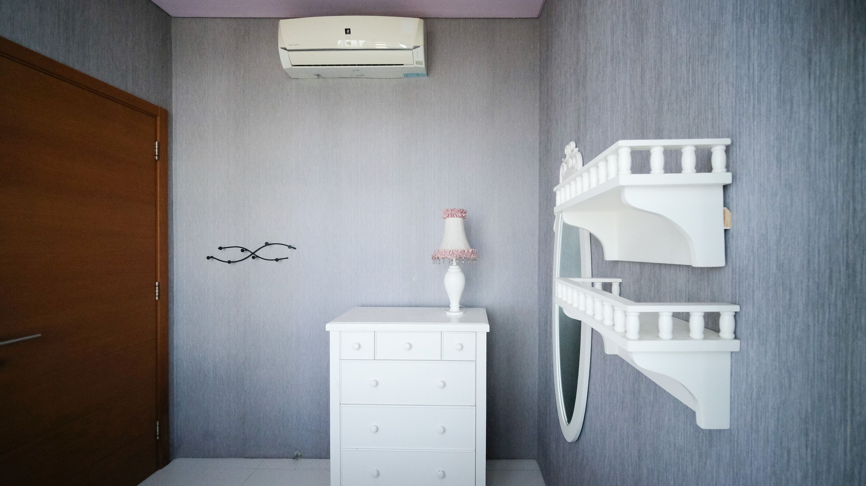A bathroom with a white dresser, a wall-mounted air conditioner, a decorative wall piece, and a white shelf unit.