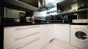 A compact kitchen with white cabinets, a black countertop, a coffee maker, a microwave, and a washing machine. - Spacious And Comfy 2Br Apartment At Aryaduta Residence Surabaya (Surabaya)