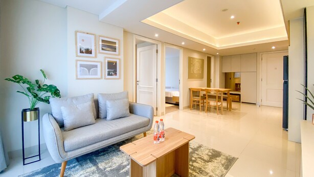 A modern living room with a sofa, coffee table, and a dining area with a table and chairs. - Best Deal And Strategic 2Br Marquis De Lafayette Apartment (Semarang)