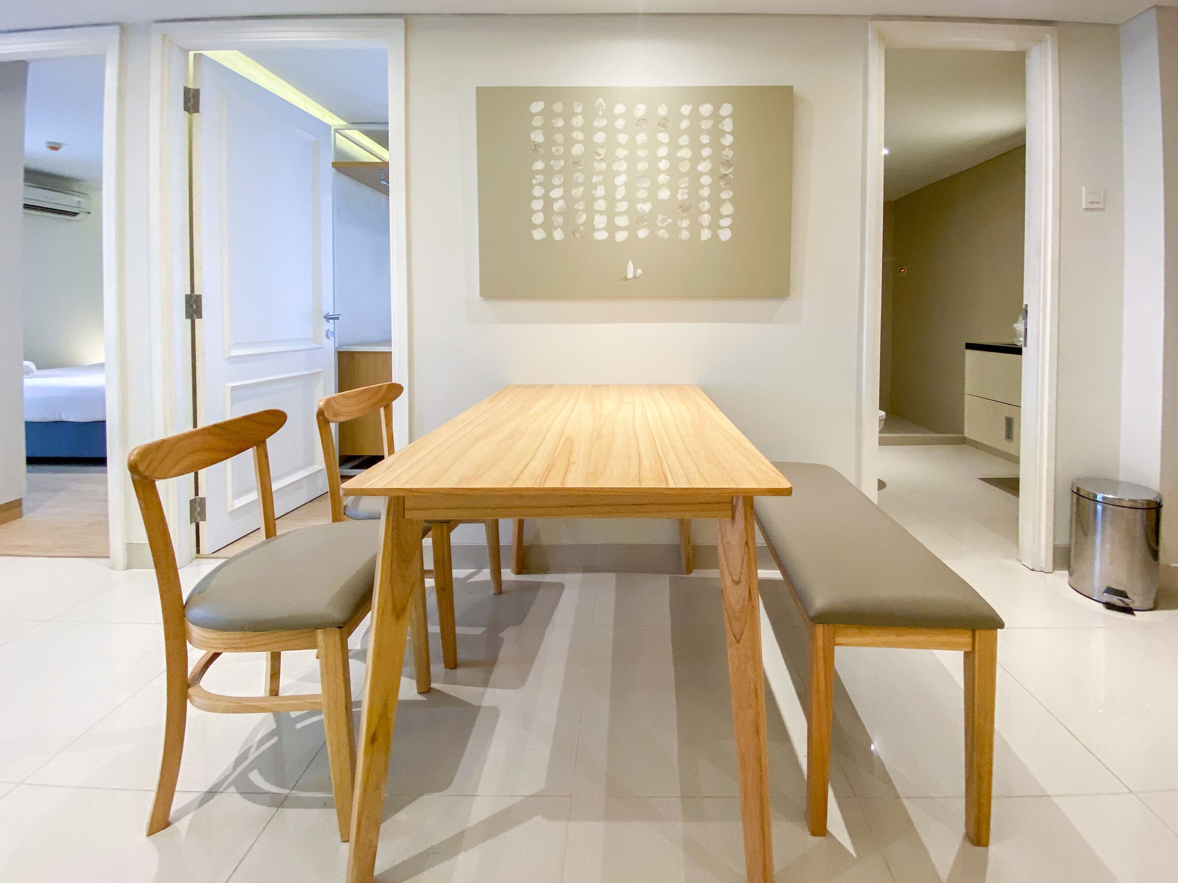 A dining area with a wooden table and four chairs, a wall art piece, and a trash can.