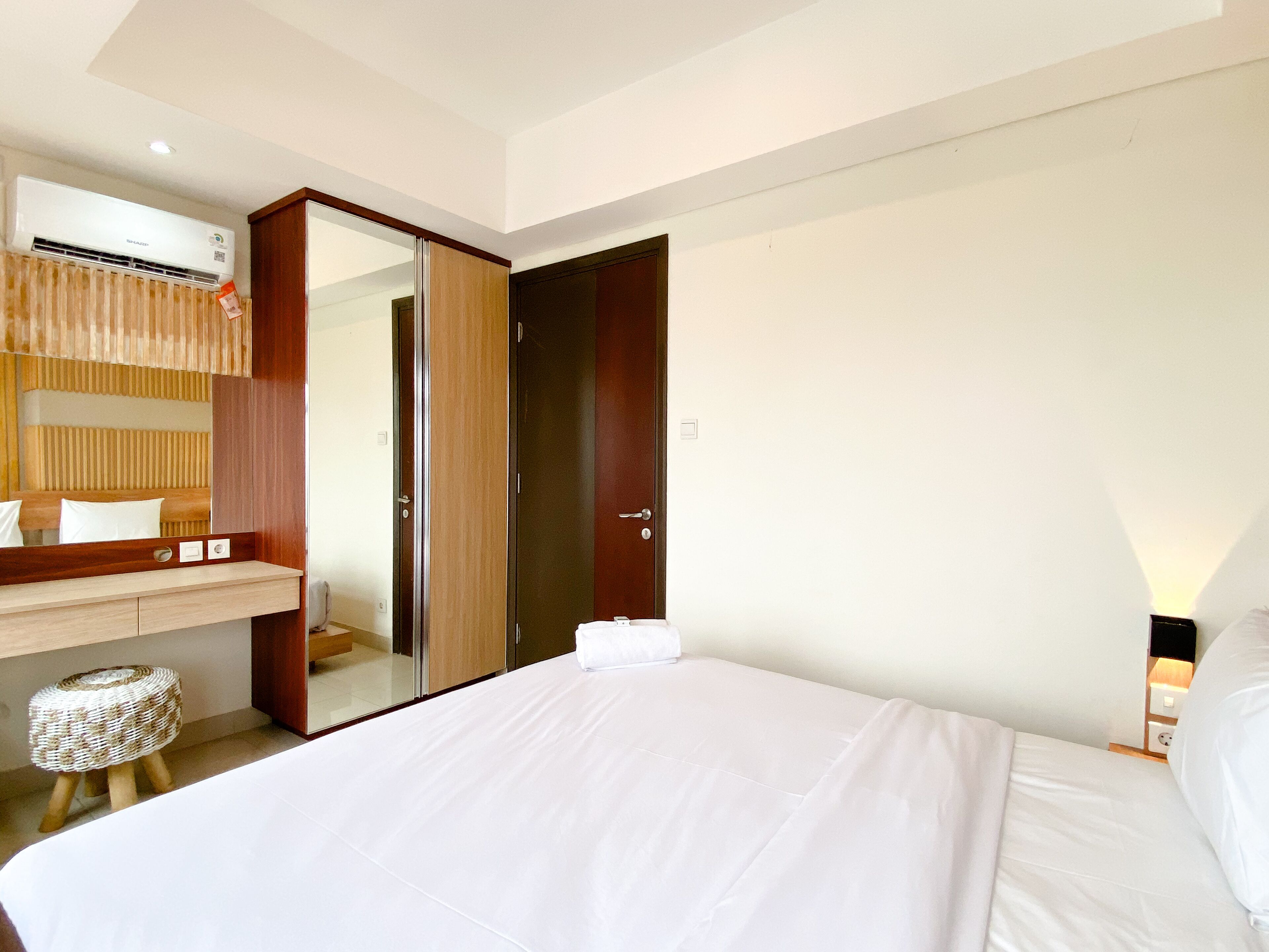 A hotel room with a bed, a wooden nightstand, a mirror, a wardrobe, and a wall-mounted air conditioner.