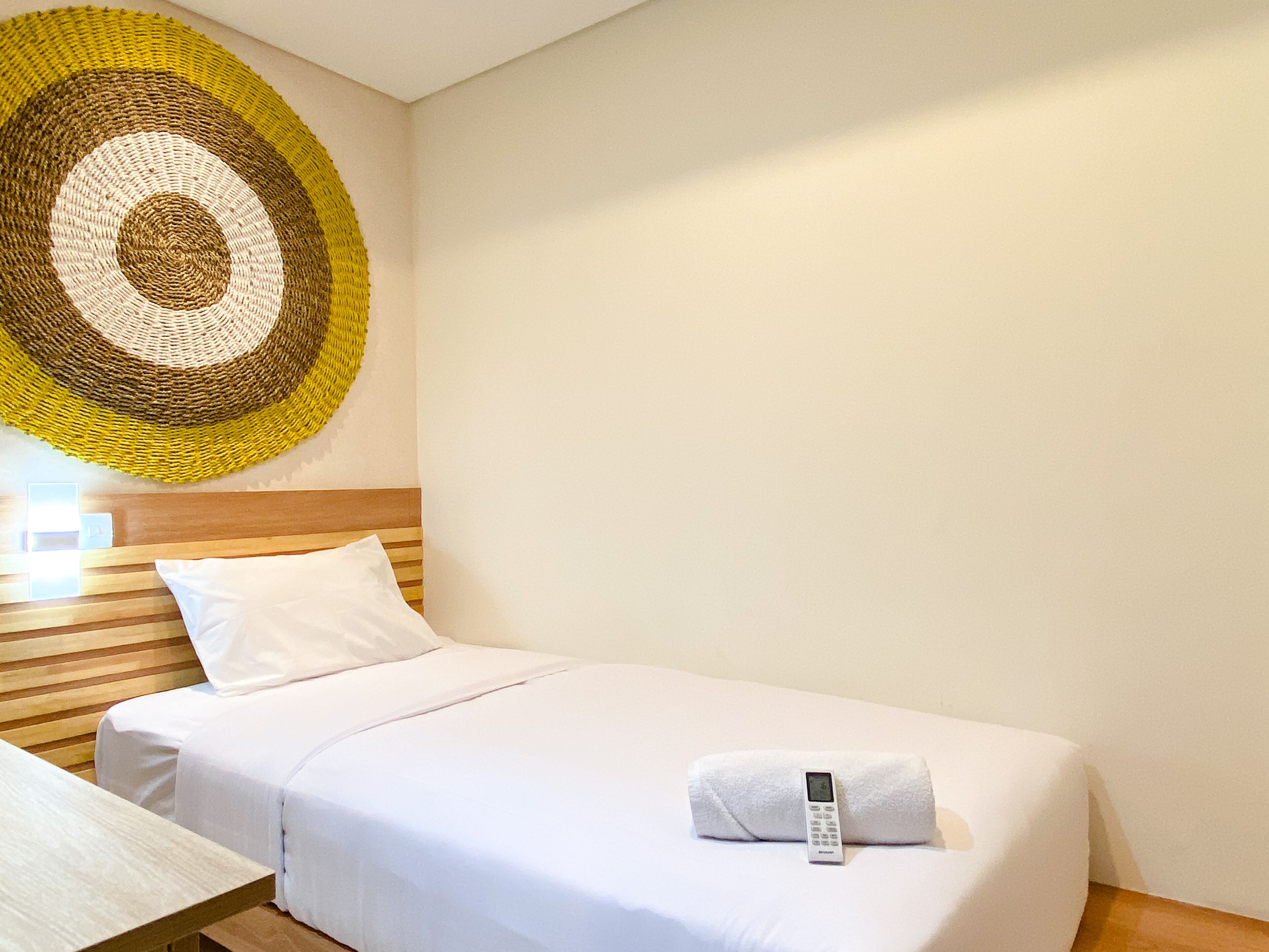 A neatly made bed with white linens and a white pillow, a wooden headboard, and a wall-mounted woven artwork.