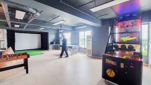 A spacious room with a foosball table, a basketball arcade game, and a large screen. - Warm Studio At 38Th Floor Sky House Alam Sutera Apartment (Tangerang)