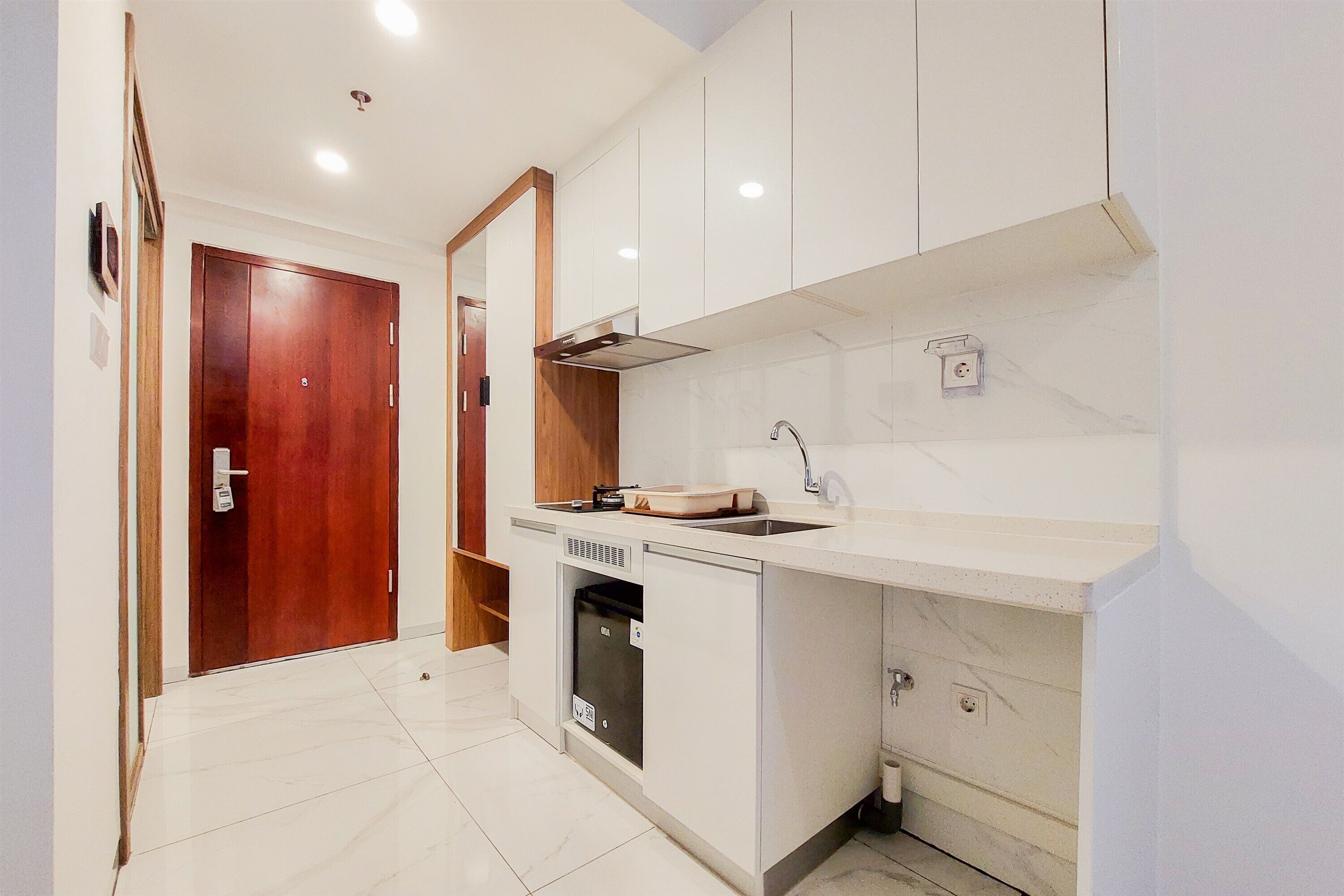 A compact kitchen with white cabinetry, a built-in dishwasher, and a wooden door.