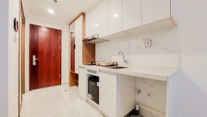 A compact kitchen with white cabinetry, a built-in dishwasher, and a wooden door. - Warm Studio At 38Th Floor Sky House Alam Sutera Apartment (Tangerang)