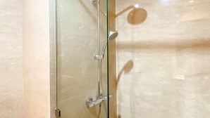 Une douche fermée par des parois en verre, dotée d’un pommeau de douche à main et d’un robinet mural.