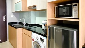 Une cuisine compacte équipée d’un réfrigérateur en acier inoxydable, d’un four à micro-ondes, d’un lave-linge et de meubles de rangement en bois.