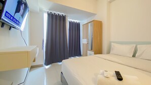 A hotel room with a bed, a TV mounted on the wall, a bedside table, and a window with curtains. - Fully Furnished And Modern Studio At Tokyo Riverside Apartment Pik 2 (Teluknaga)