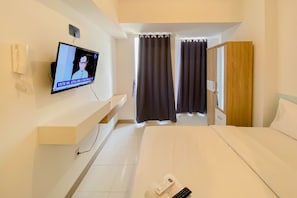A hotel room with a bed, a TV mounted on the wall, a bedside table, a nightstand, and a window with curtains.
