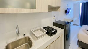 A modern kitchen with a stainless steel sink, a small container of sugar, a black coffee machine, and a TV mounted on the wall. - Fully Furnished And Modern Studio At Tokyo Riverside Apartment Pik 2 (Teluknaga)