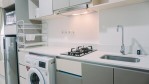 A modern kitchen with a built-in washing machine, a gas stove, and a sink. - Homey And Warm Studio At 28Th Floor Gold Coast Apartment (Jakarta)