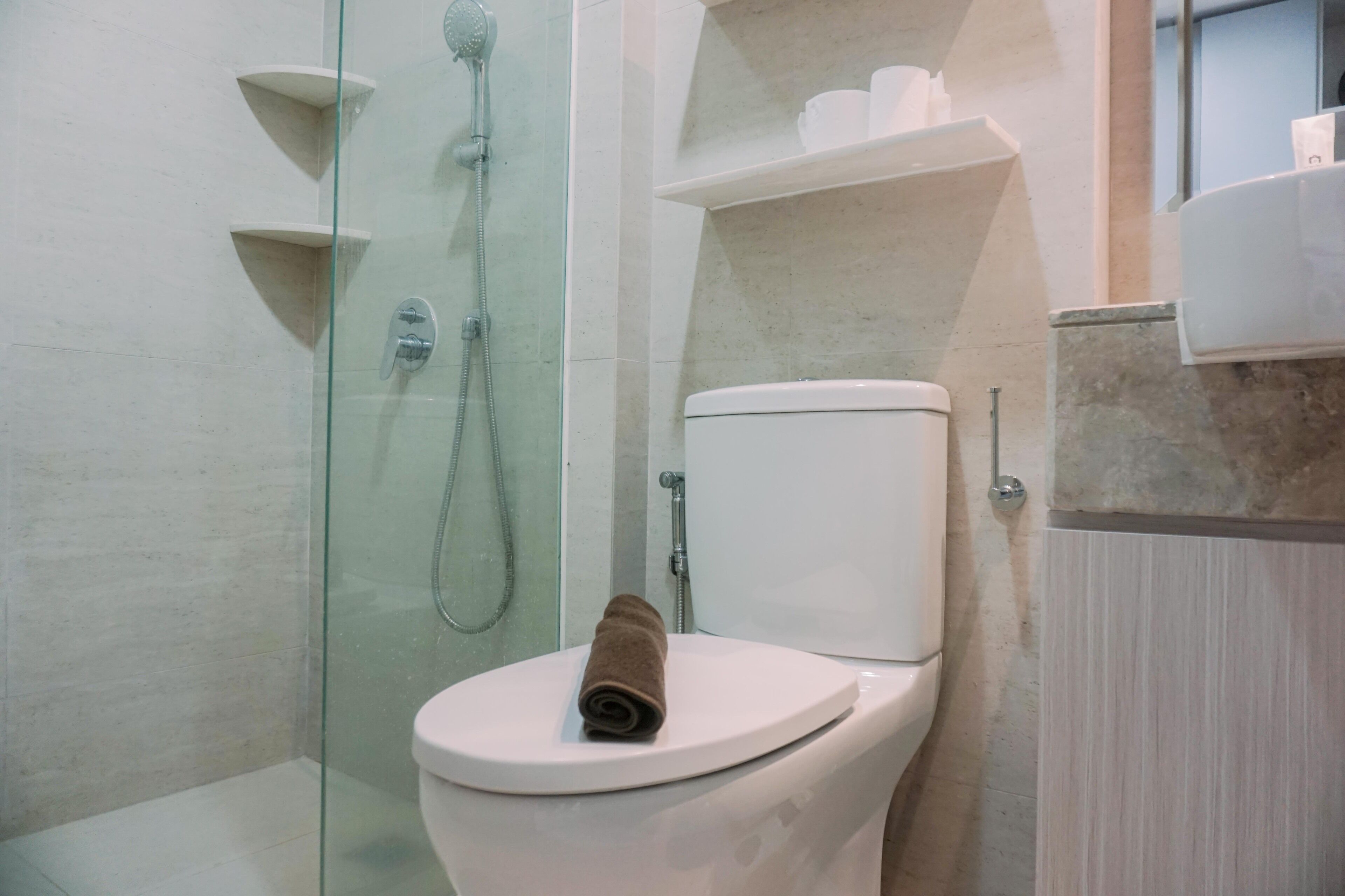A modern bathroom with a glass-enclosed shower, a white toilet, and a marble-topped sink.