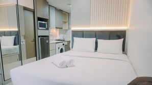 A modern hotel room with a neatly made bed, a microwave, a washing machine, and a small kitchenette. - Homey And Warm Studio At 28Th Floor Gold Coast Apartment (Jakarta)
