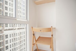 Una habitación con un tendedero de madera junto a una pared blanca, ventanas amplias con vistas a un edificio de gran altura.