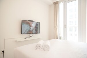 Una habitación de hotel con una cama, un televisor montado en la pared y una ventana con cortinas.