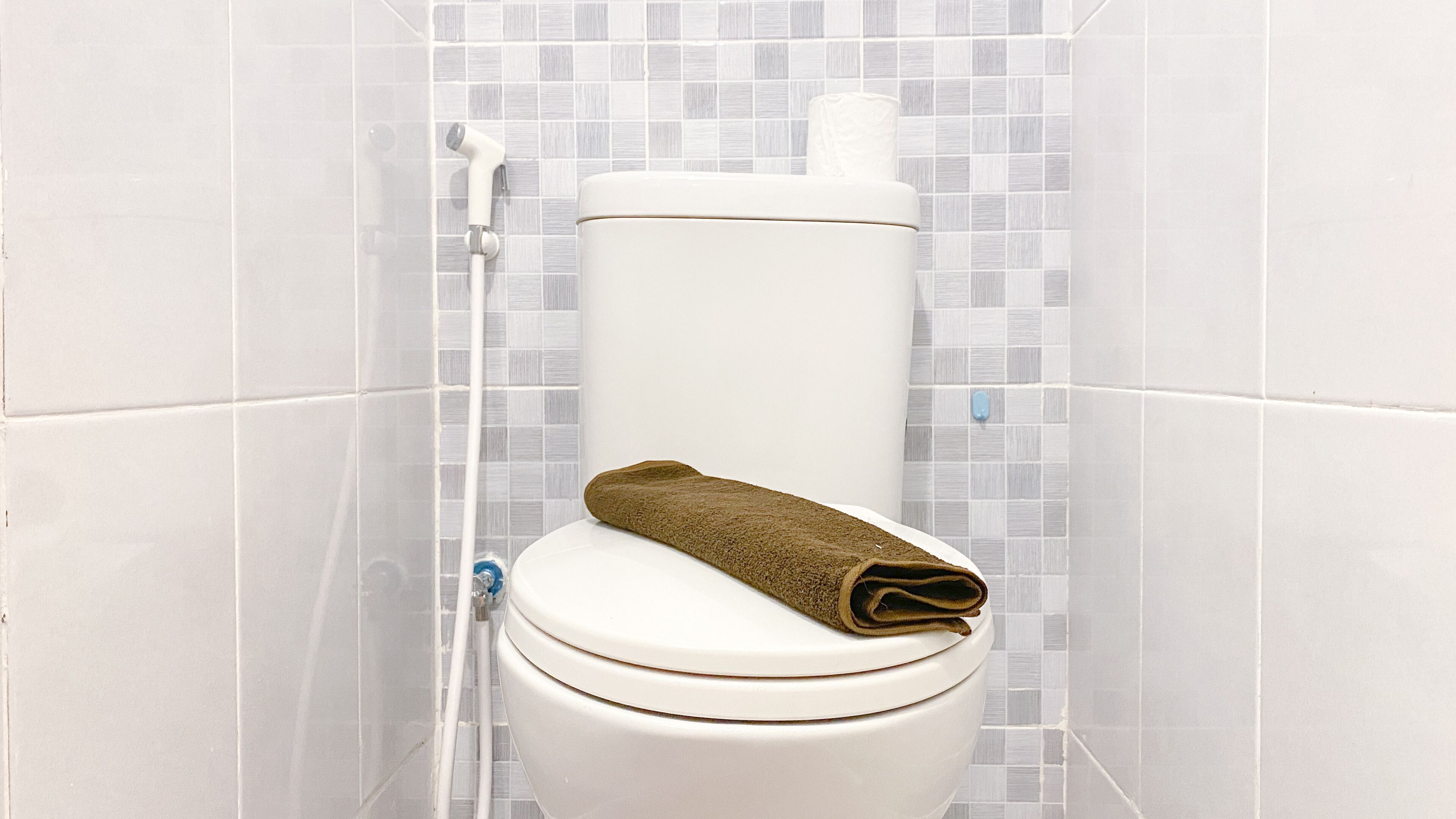A white toilet with a brown towel on the seat, set against a tiled wall with a grid pattern.