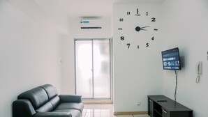 A modern living room with a black leather sofa, a flat-screen TV mounted on the wall, and a sliding glass door leading to a balcony. - Good Choice 2Br Apartment M-Town Residence (Gading Serpong)