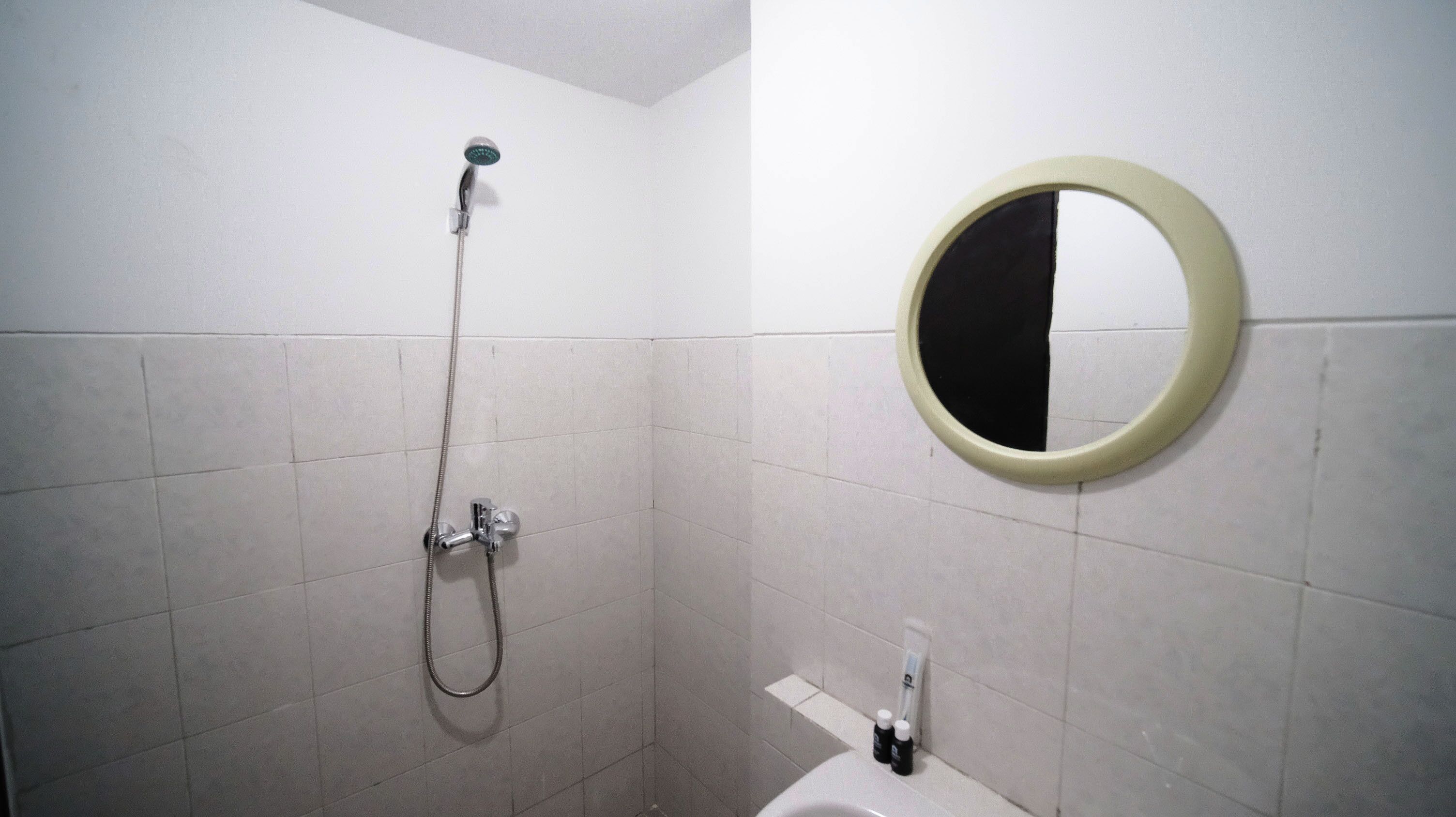 A bathroom with a shower, a toilet, and a round mirror on the wall.