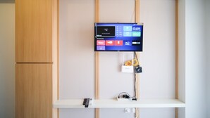 A flat-screen TV mounted on a wall with a remote control on a shelf below. - Simple And Tidy Studio Apartment At Suncity Residence (Sidoarjo)