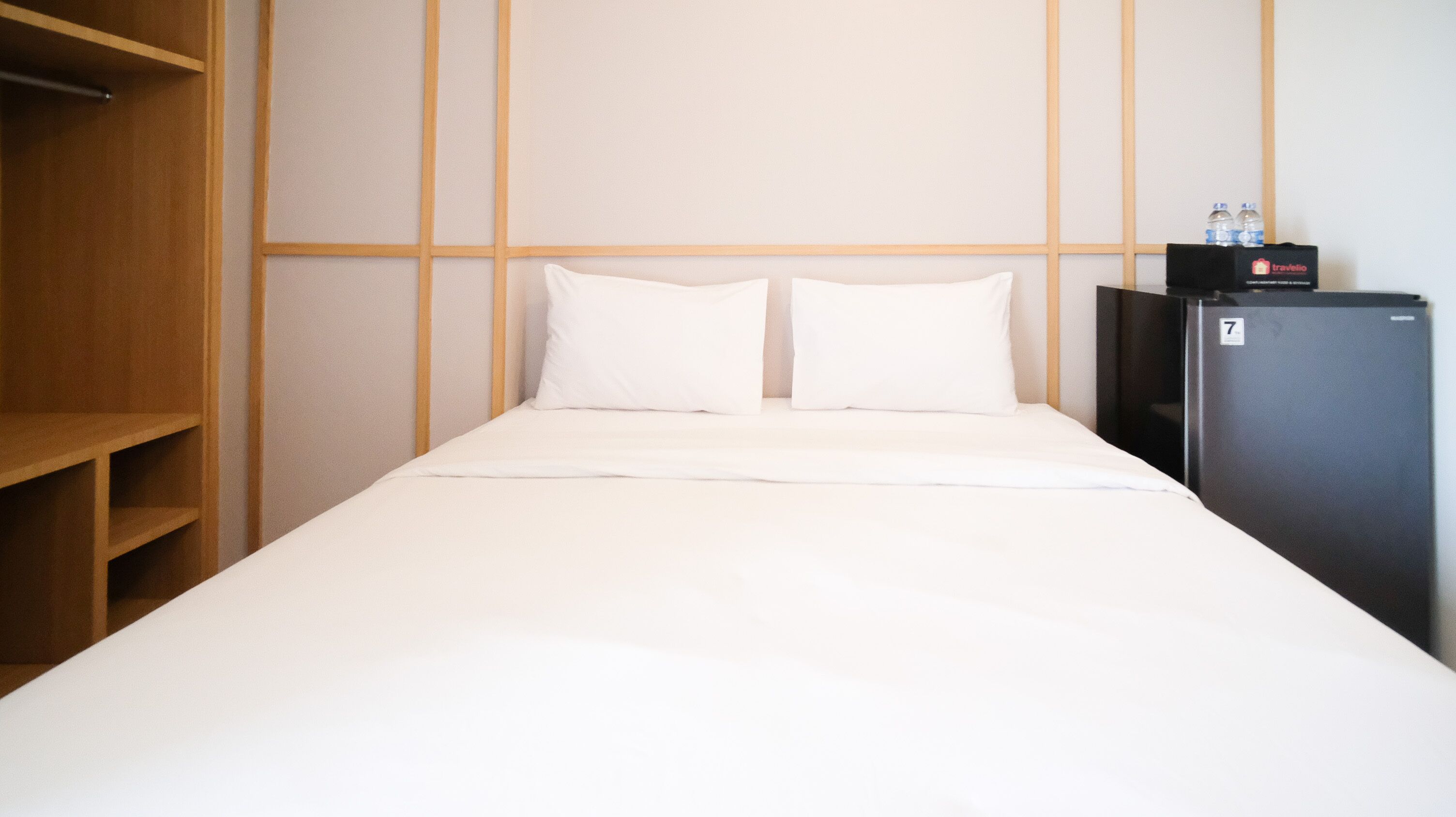 A hotel room with a bed, two pillows, a wardrobe, and a refrigerator.