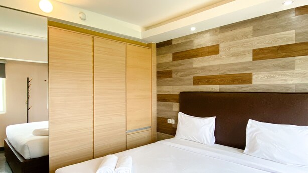A modern hotel room with a large bed, wooden wardrobe, and a wall with wooden panels. - Best Deal And Homey 1Br Apartment Grand Sentraland Karawang (Karawang)