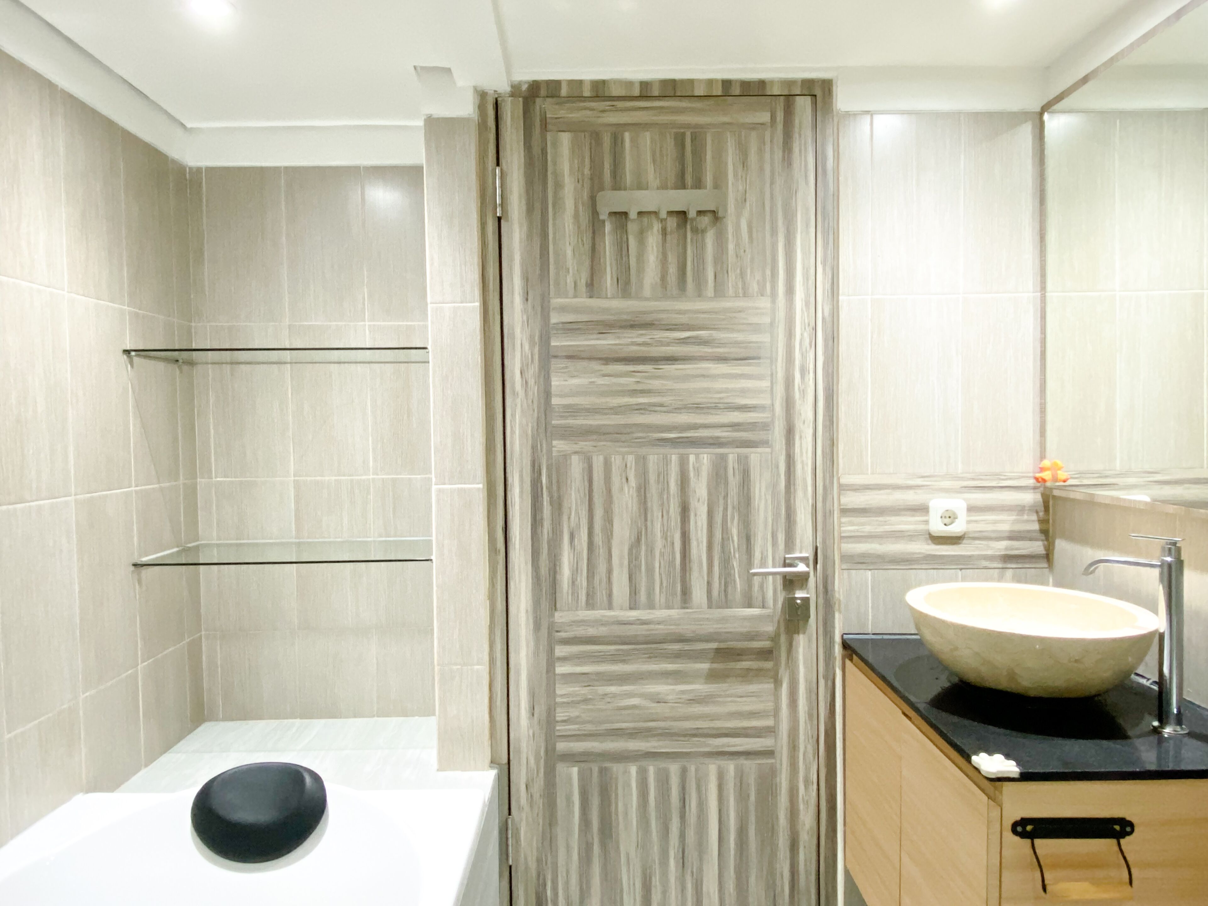 Een moderne badkamer met een houten deur, een witte wastafel met een zwarte kom en een spiegel boven de wastafel.