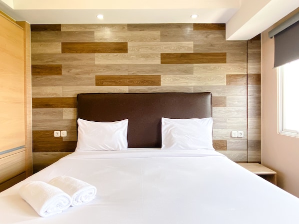 A hotel room with a modern design, featuring a wooden wall panel and a large bed with white linens.