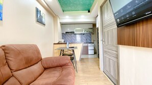 A living room with a brown sofa, a dining table, and a kitchen in the background. - Best Deal And Homey 1Br Apartment Grand Sentraland Karawang (Karawang)