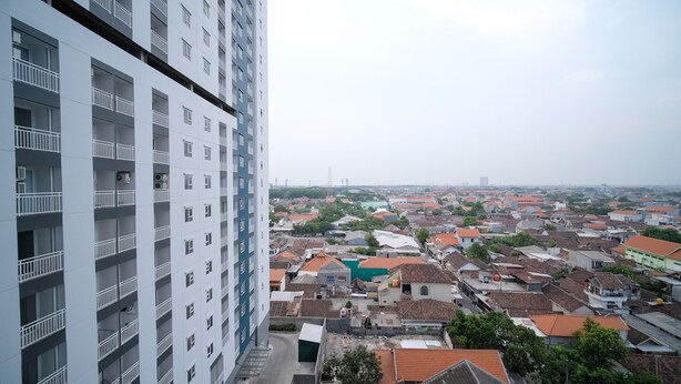 Un edificio de gran altura con múltiples balcones y vistas a una zona urbana densamente poblada, con diversos edificios y zonas verdes.