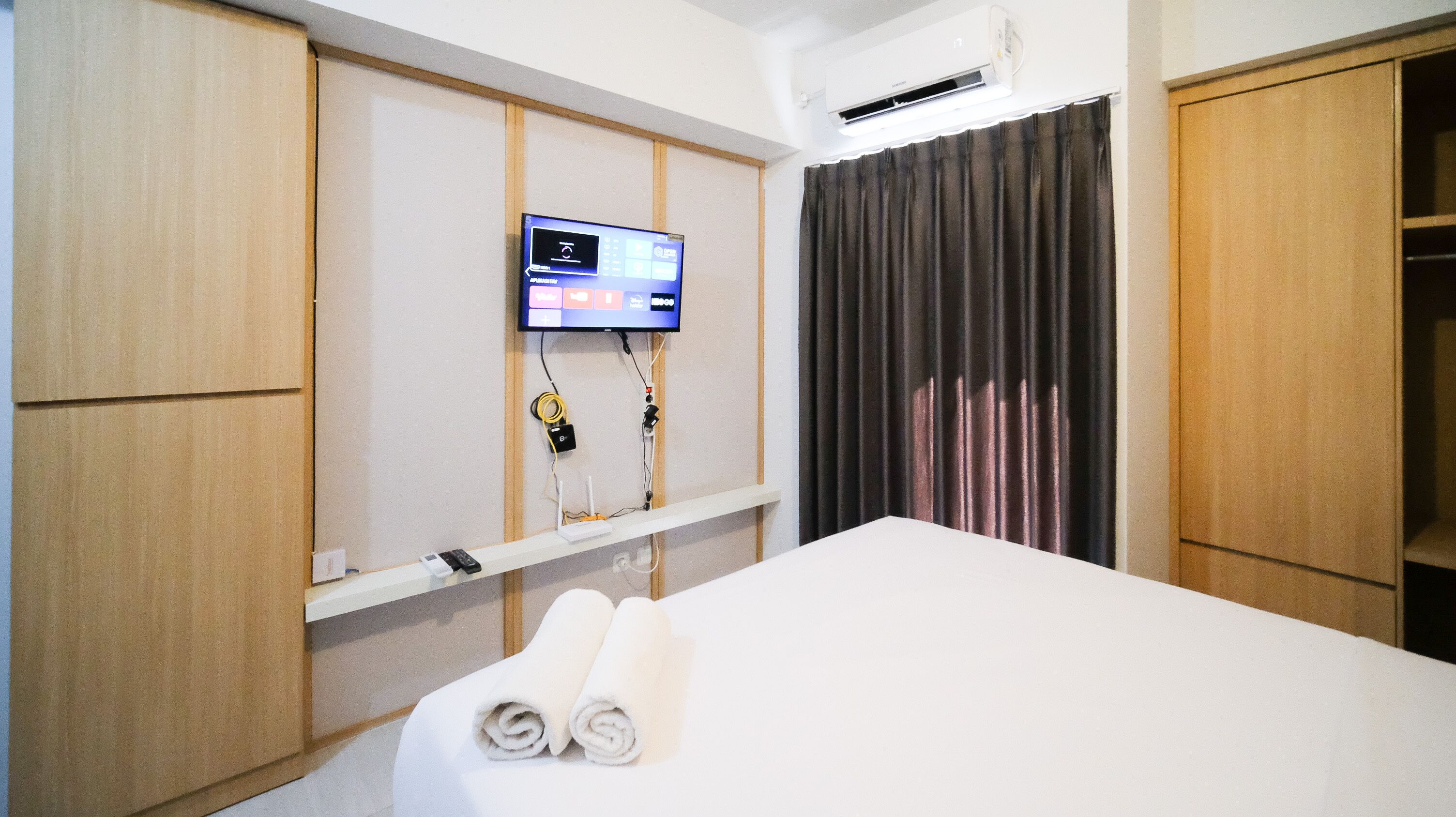 Una habitación de hotel con una cama, un televisor montado en la pared y una cortina.