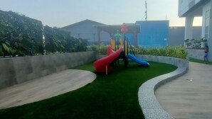 A playground with two slides and a climbing structure, surrounded by green artificial grass and concrete pathways. - Good Location And Best Deals Studio Apartment At Suncity Residence (Sidoarjo)
