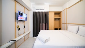 A hotel room with a bed, a TV mounted on the wall, a wardrobe, and a curtain. - Good Location And Best Deals Studio Apartment At Suncity Residence (Sidoarjo)