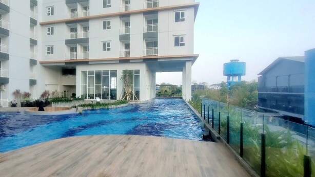 A modern building with a swimming pool, a covered area, and a water tower in the background. - Good Location And Best Deals Studio Apartment At Suncity Residence (Sidoarjo)