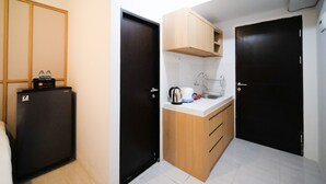 A compact kitchenette with a refrigerator, a sink, and wooden cabinets. - Good Location And Best Deals Studio Apartment At Suncity Residence (Sidoarjo)