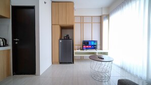 A modern kitchen with a refrigerator, a coffee machine, and a flat-screen TV on a stand. - Comfy And Spacey 2Br Apartment At Suncity Residence (Sidoarjo)