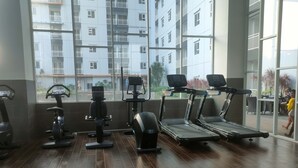 A gym with exercise equipment, large windows, and a view of a residential building. - Comfy And Spacey 2Br Apartment At Suncity Residence (Sidoarjo)