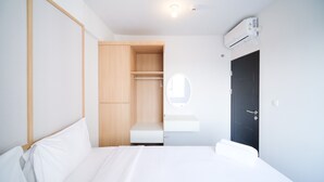 A modern hotel room with a bed, a wooden wardrobe, a mirror, and an air conditioning unit. - Comfy And Spacey 2Br Apartment At Suncity Residence (Sidoarjo)